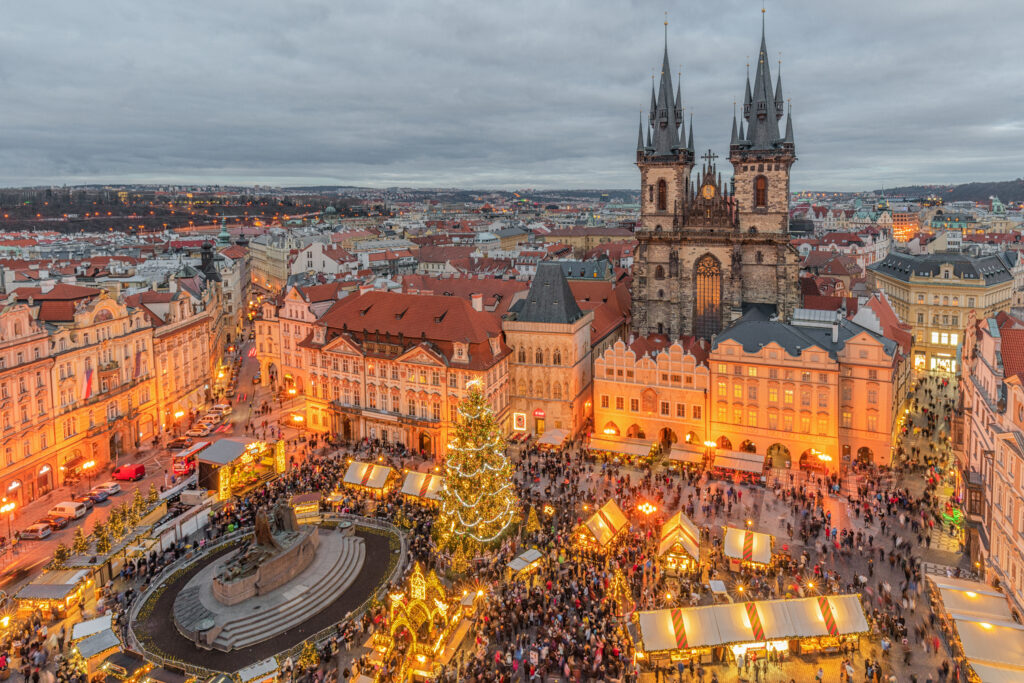 Vista al atardecer de la Plaza de la Ciudad Vieja de Praga durante el mercado navideño, con la iluminada Iglesia de Nuestra Señora de Týn alzándose sobre los puestos festivos del mercado en Praga, República Checa.