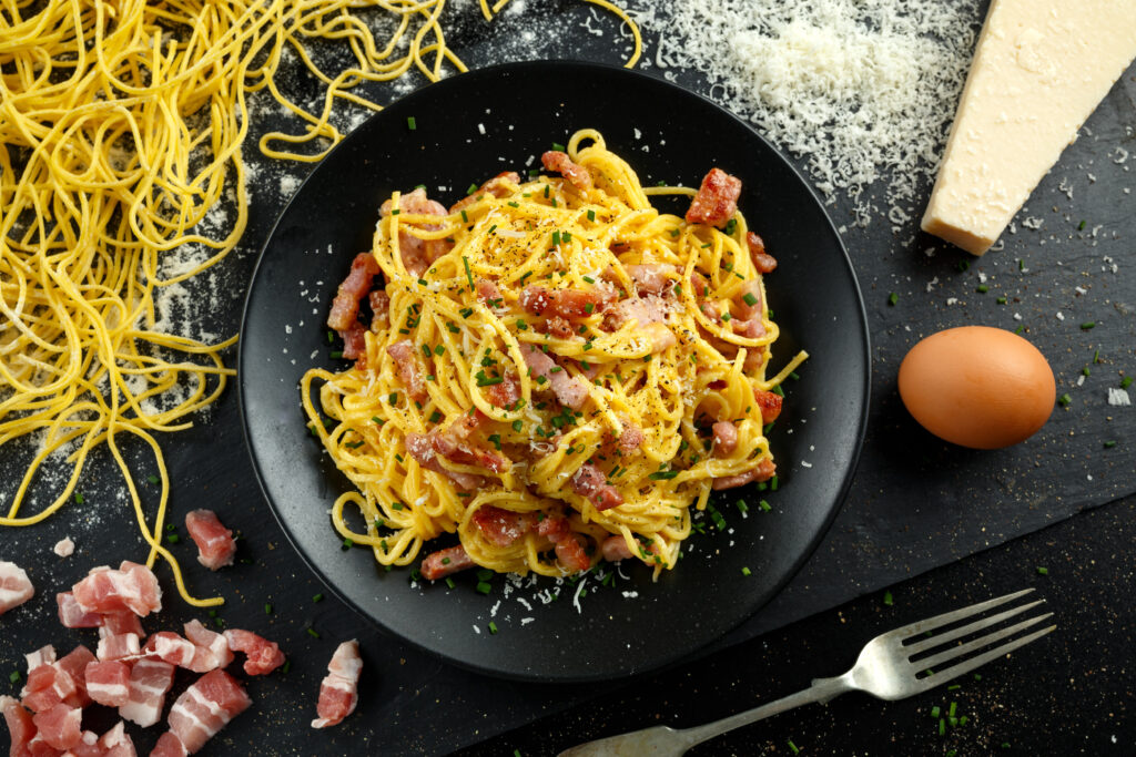Pasta carbonara italiana casera clásica con panceta, huevos y queso parmesano en un plato negro.