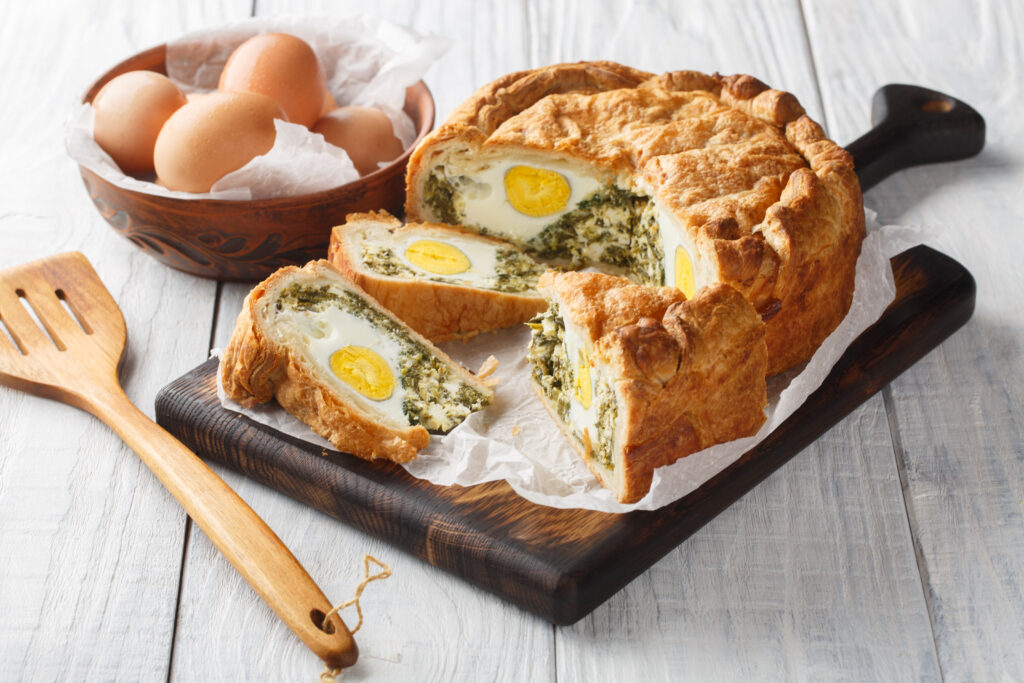 Torta Pasqualina, una especialidad típica de pastel salado de Pascua de Liguria; primer plano de la torta sobre una tabla de madera en la mesa. Orientación horizontal.