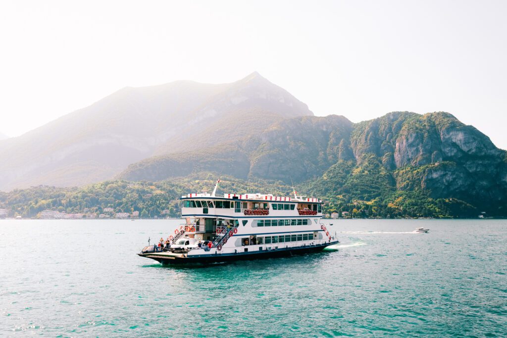 El tranquilo lago de Como (en italiano, *Lago di Como*). Transporte en grandes transbordadores para vehículos y pasajeros en un puerto impresionante. Pequeña localidad turística costera en los Alpes. Panorama pintoresco. Embarcación. Bosques y colinas.